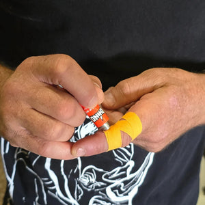Close-up of hands applying super glue to orange zinc oxide tape.